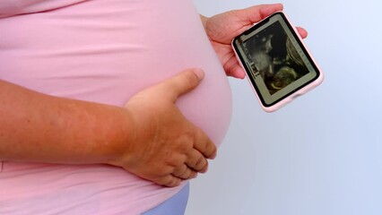 Poster - pregnant woman holds mobile phone with ultrasound screen examination, small child rolls over in mother's belly, concept pregnancy reproduction, healthcare pregnancy, happy motherhood, selective focus