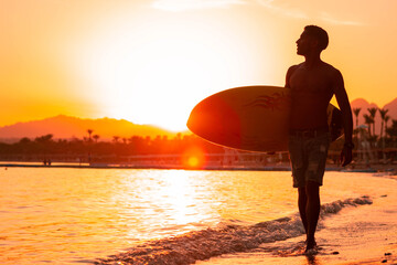 Silhouette man surfer in sunset light walking down beach with surfboard near waters edge enjoying summer time practice hobby during getaway vacations, guy recreating at tropical island with waves