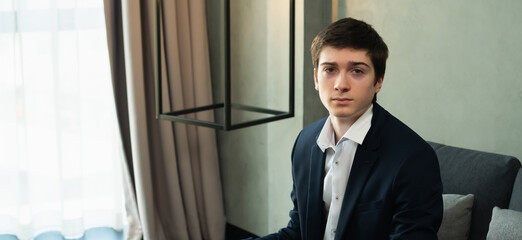 caucasian businessman wear suit, sit on sofa, looking at camera. Young man work business with home office background and copy space