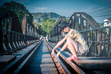 Female Asian Tourist Is Sitting On The Old Train Track Of River Kwai Historical Site In Kanchanaburi, Thailand.