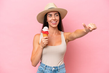 Wall Mural - Young caucasian woman with a cornet ice cream isolated on pink background giving a thumbs up gesture