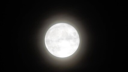 Wall Mural - Glowing huge full moon as seen from earth through the clouds against starry night sky. Large full moon moves across the sky, moon makes its way from bottom left frame to top right.