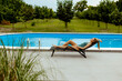 Young woman lying on a deck char by the swimming pool in the house backyard