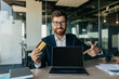 © Prostock-studio - Happy businessman holding credit card and pointing at laptop screen with empty screen, sitting in office, mockup