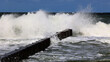 Duża morska fala rozbija się o falochron  na wybrzeżu