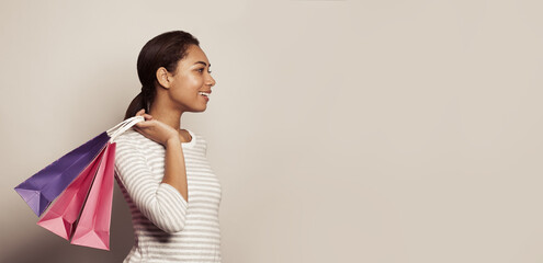 Wall Mural - Cute black woman holding shopping bags against white wall banner background. Shopping, sales, black friday concept.