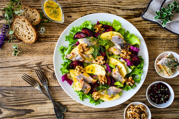 Sticker - Marinated herrings with roasted beetroots, apple, walnuts  and fresh vegetable leaves on wooden table
