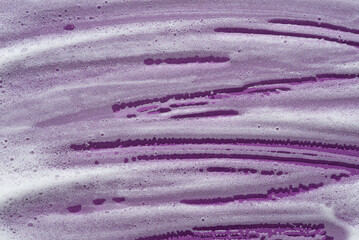 Wall Mural - Foam swatch on a violet background. Soapy liquid texture with bubbles. Natural sunshine and shadows. Skin care cleansing cosmetic in top view.