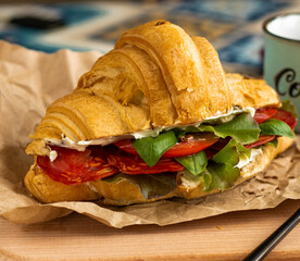 Tasty breakfast. Appetizing croissant with salami and, cheese and tomatoes. homemade croissant with salty filling, bacon, lettuce and fresh tomato. quick snack, lunch