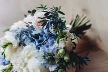 A Beautiful Wedding Bouquet Of White, Blue And Pale Pink Flowers Lies On The Table