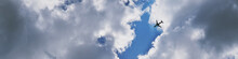 The Passenger Airplane Is Flying Far Away In The Blue Sky And Clouds. Dramatic Clouds Backlit By The Sun. Aircraft In The Air. Banner Or Header. International Passenger Air Transportation