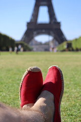 Man's feet wearing red espadrilles on the lawn in front of the Eiffel Tower in Paris