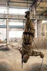 A soldier in camouflage trains fast military rappels upside down with a gun upside down with a gun. Preparation of an anti-terrorist operation.