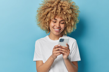 Wall Mural - photo of good looking woman with curly hair uses mobile phone for chatting online and networking smi