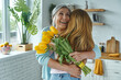 © gstockstudio - Happy senior woman embracing her daughter and holding a bunch of yellow tulips
