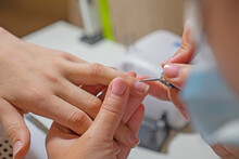 Manicurist Master Removing Cuticles. Processing Of Rough Cuticles And Lateral Folds Of Nails On Hands With A Conical Instrument. Medical Hardware Manicure In A Beauty Salon