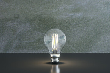 Wall Mural - Close up of illuminated light bulb with filament on chalkboard wall background. New idea and innovation concept. 3D Rendering.