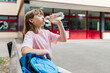© Elena Medoks - A schoolgirl sits in the school yard and drinks fresh water from a bottle. Water balance of children during school hours. Back to school concept