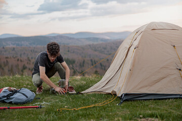 Wall Mural - Caucasian young man setting tent on top of mountain. Beautiful view. Summer tourism.