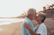 © Daniel - Close up of two cute and happy seniors having fun and enjoying together a sunset day at the beach. Mature couple in love kissing together with the sunset at the background..