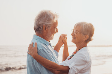 Wall Mural - Couple of old mature people dancing together and having fun on the sand at the beach enjoying and living the moment. Portrait of seniors in love looking each others having fun.