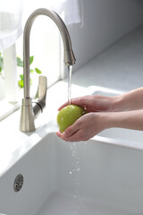 Wall Mural - Woman washing apple over sink in kitchen, closeup