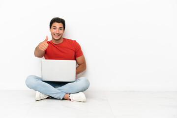 Wall Mural - Caucasian handsome man with a laptop sitting on the floor with thumbs up because something good has happened