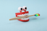 Fototapeta  - Funny toy clockwork jumping teeth with eyes and toothbrush on blue background.