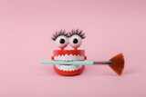 Fototapeta  - Funny toy clockwork jumping teeth with eyes and false eyelashes holding makeup brush on pink background. Beaty concept