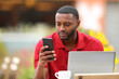 © Antonioguillem - Black man in red using phone and laptop in a terrace