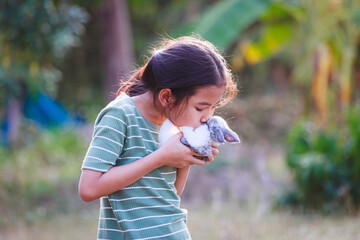 Wall Mural - Asian child girl holding and hugging her adorable bunny fluffy with tenderness and love. Kid take care and play with pet in the garden. Symbol of Easter day.