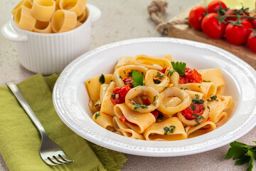 Poster - Italian pasta with calamari and tomato sauce. Calamarata is a kind of thick ring pasta paccheri, with sliced squid. Originates from Naples, the South of Italy. Raw paccheri on background.