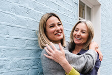 Happy Young Woman Embracing Mother In Front Of Blue Wall