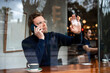 © Westend61 - Businessman talking on smart phone touching glass window of cafe