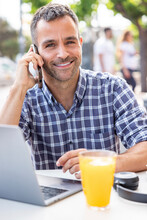 Smiling Freelancer Talking On Mobile Phone At Sidewalk Cafe