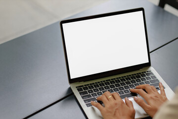woman using and typing on laptop computer with blank white desktop screen on wooden table