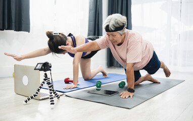 Concept Elderly exercise at home, Asian elderly woman and Asian teenage woman exercising in living room by video guide from laptop and recording video with camera.