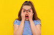 © Red Cristal - Amazed brunette girl covering face with hands and peeping through her fingers at camera. Young attractive female hiding her face being frightened, scared or ashamed, standing over yellow background