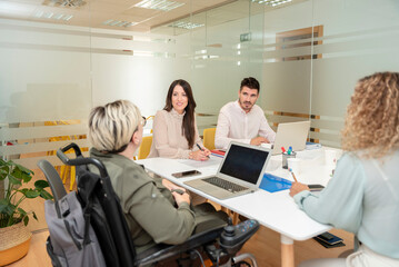 young people in a boardroom listening to the female leader seated in a wheelchair.