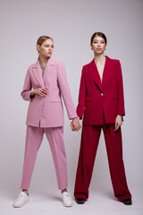 Wall Mural - Two fashion asian and european models in soft pink and red oversized suits, jacket, pants, sneakers.  Beautiful young women. Studio shot, portrait. White gray background.