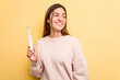 Young caucasian woman holding a electric toothbrush isolated on yellow background looks aside smiling, cheerful and pleasant.