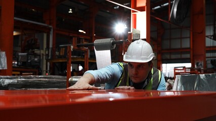 Engineer man wearing green uniform and safety white helmet under inspection and checking production process on factory station. Warehouse workshop for factory operators at metal industry factory.