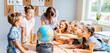 © Iryna - Happy cute enthusiastically pupils smiling around a globe in classroom with female teacher at school. Group of curious classmates at workplace studying globe in classroom.