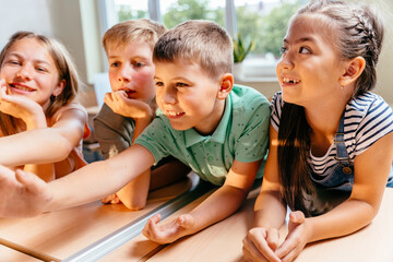 Canvas Print - Group of children in a row enthusiastically work at the class. Cute pupils study in classroom. Friendship, interaction teamwork concept.