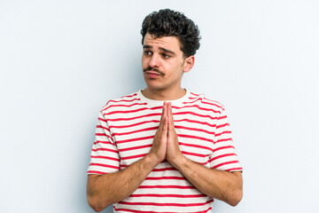 Young caucasian man isolated on blue background praying, showing devotion, religious person looking for divine inspiration.