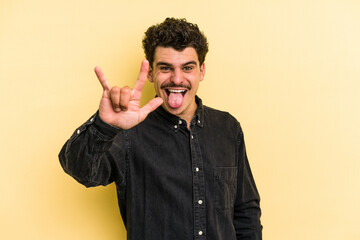 Wall Mural - Young caucasian man isolated on yellow background showing a horns gesture as a revolution concept.