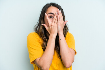 Wall Mural - Young caucasian woman isolated on blue background blink through fingers frightened and nervous.