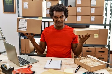 Sticker - African man with curly hair working at small business ecommerce winking looking at the camera with sexy expression, cheerful and happy face.