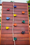 Fototapeta  - Artificial rock climbing wall. Wooden wall with rope and artificial rock for kids climbing. Playground equipment for children activity. 
