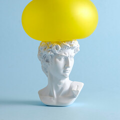 A yellow balloon presses on the head of David of an antique renaissance statue on a pastel blue background as a concept of pressure and problems.